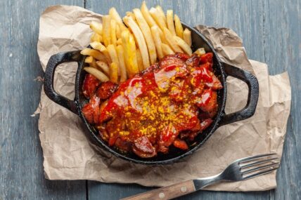 Currywurst with French fries in black skillet.