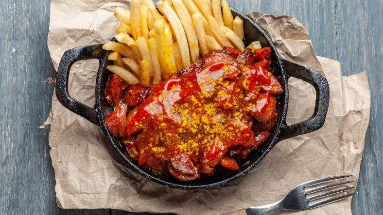 Currywurst with French fries in black skillet.